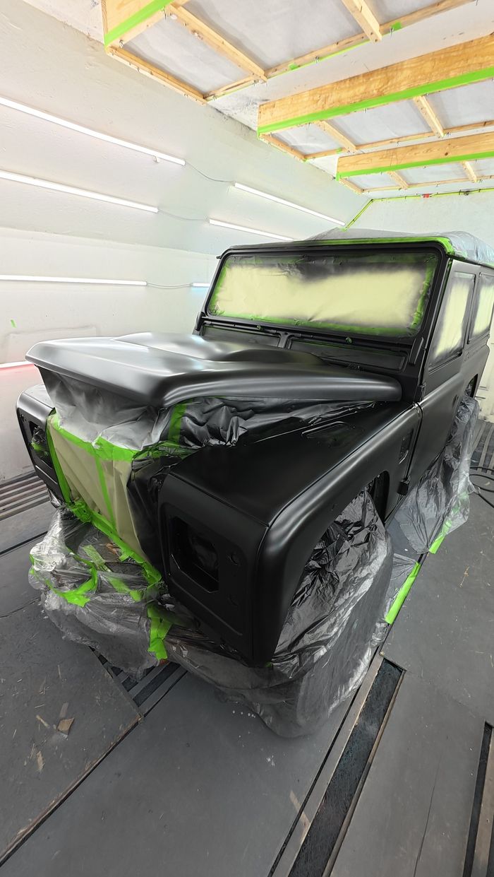 Defender in the paint booth with the dark grey coat applied over the primer, still masked
