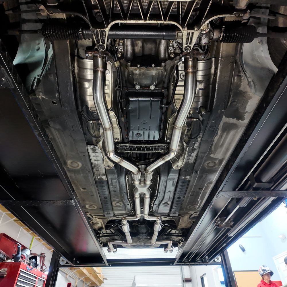 Polished stainless dual exhaust with X-pipe installed under a classic car on a lift