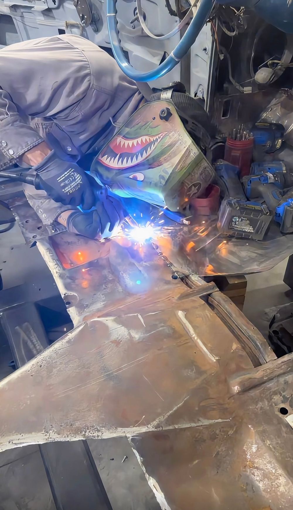 Welder in a mask MIG-welding a new panel inside a stripped car body
