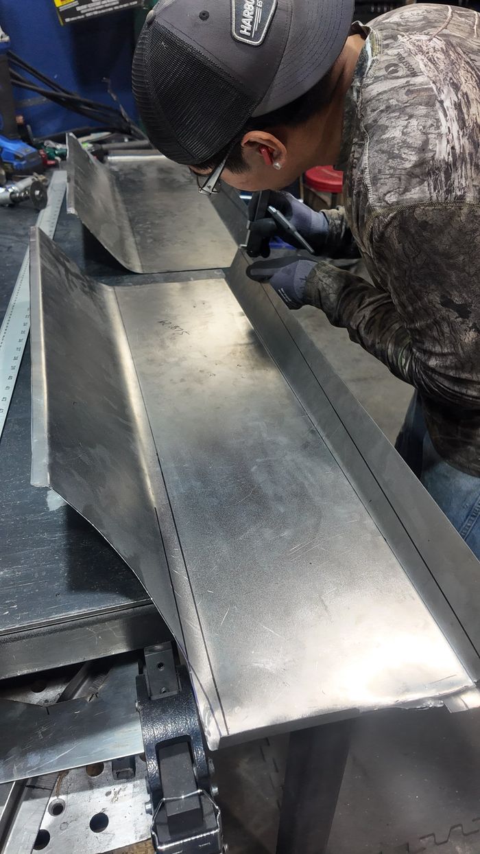 Technician checking the fit of a long fabricated sheet-metal section on the bench