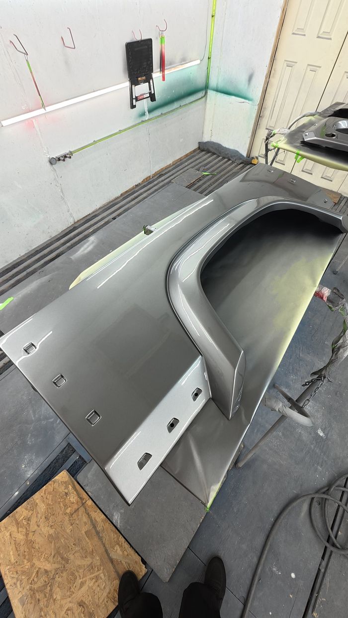Defender front fender lying on a stand in the paint booth, freshly coated in satin dark grey