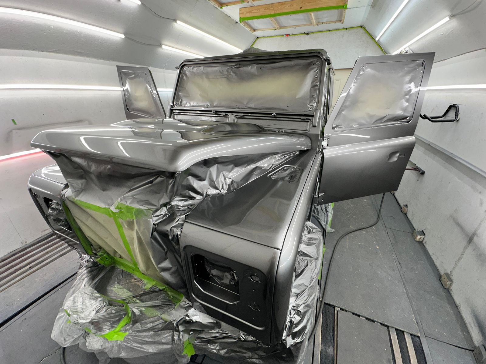 Land Rover Defender in the paint booth with doors open, freshly coated in satin dark grey, windows and interior still masked