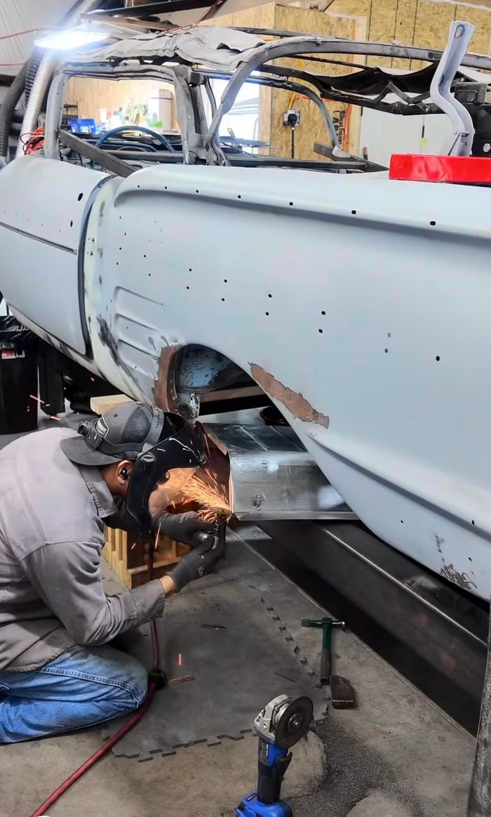 Technician grinding welds on the lower rear quarter of the primered Impala body on a rotisserie