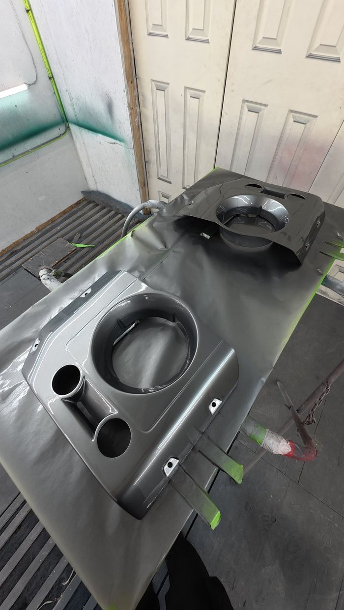 Defender headlight surround panel on a stand in the paint booth, coated in satin dark grey