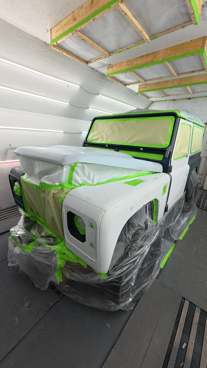 Defender masked with green tape and plastic in the paint booth, body in white primer
