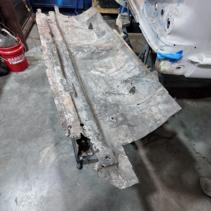 Rusted-through original trunk floor section lying on the shop floor after removal